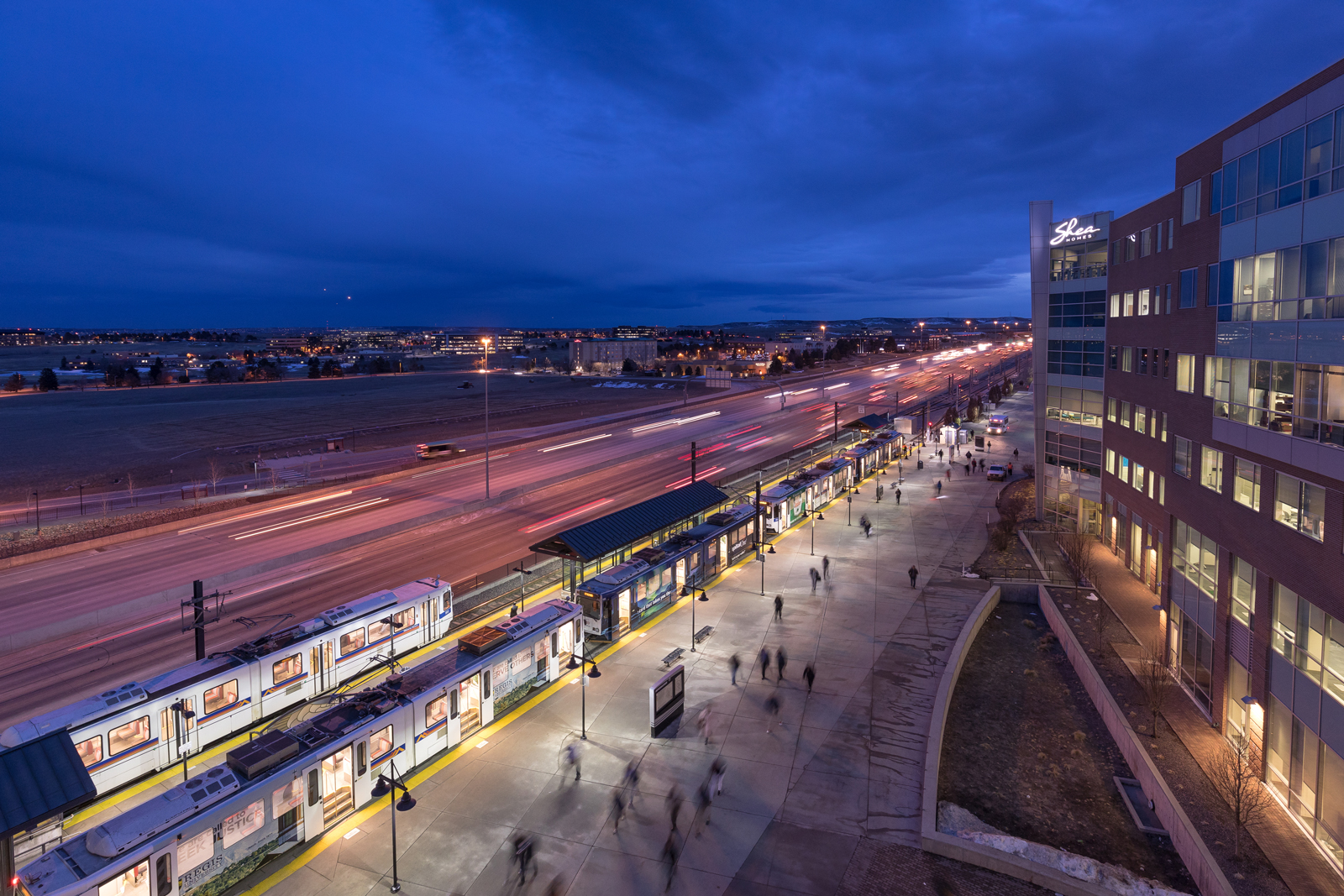 People walking around a light rail station at night with a highway in the background. Photo credit: Photo courtesy of RTD.