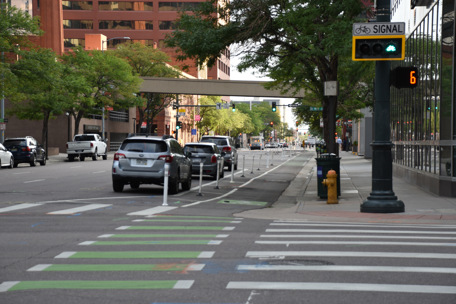 Cars parked on a city street next to a bike lane, with a bicycle traffic signal in the foreground.