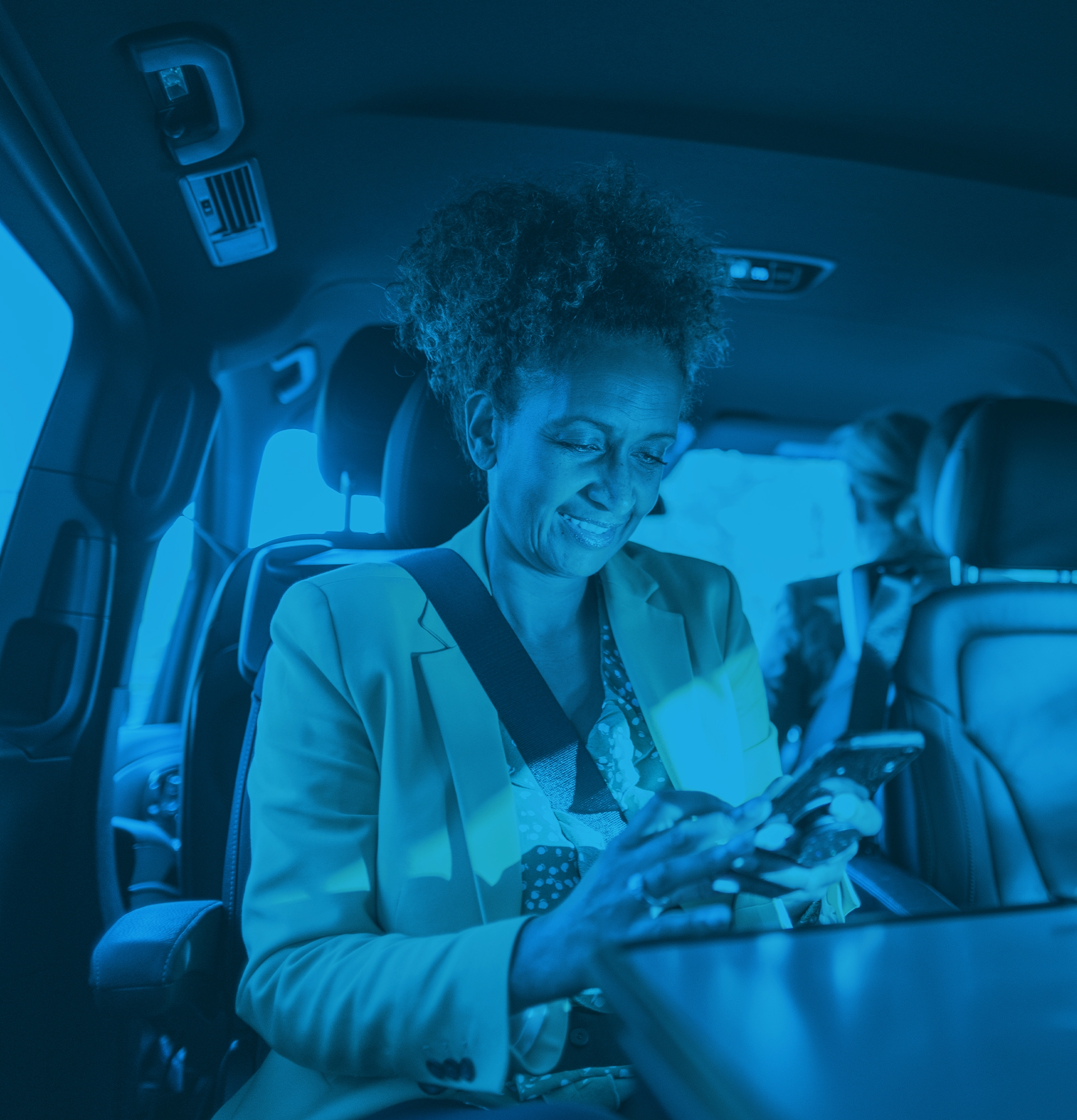 Woman wearing a seatbelt inside of a vehicle smiling and looking at phone