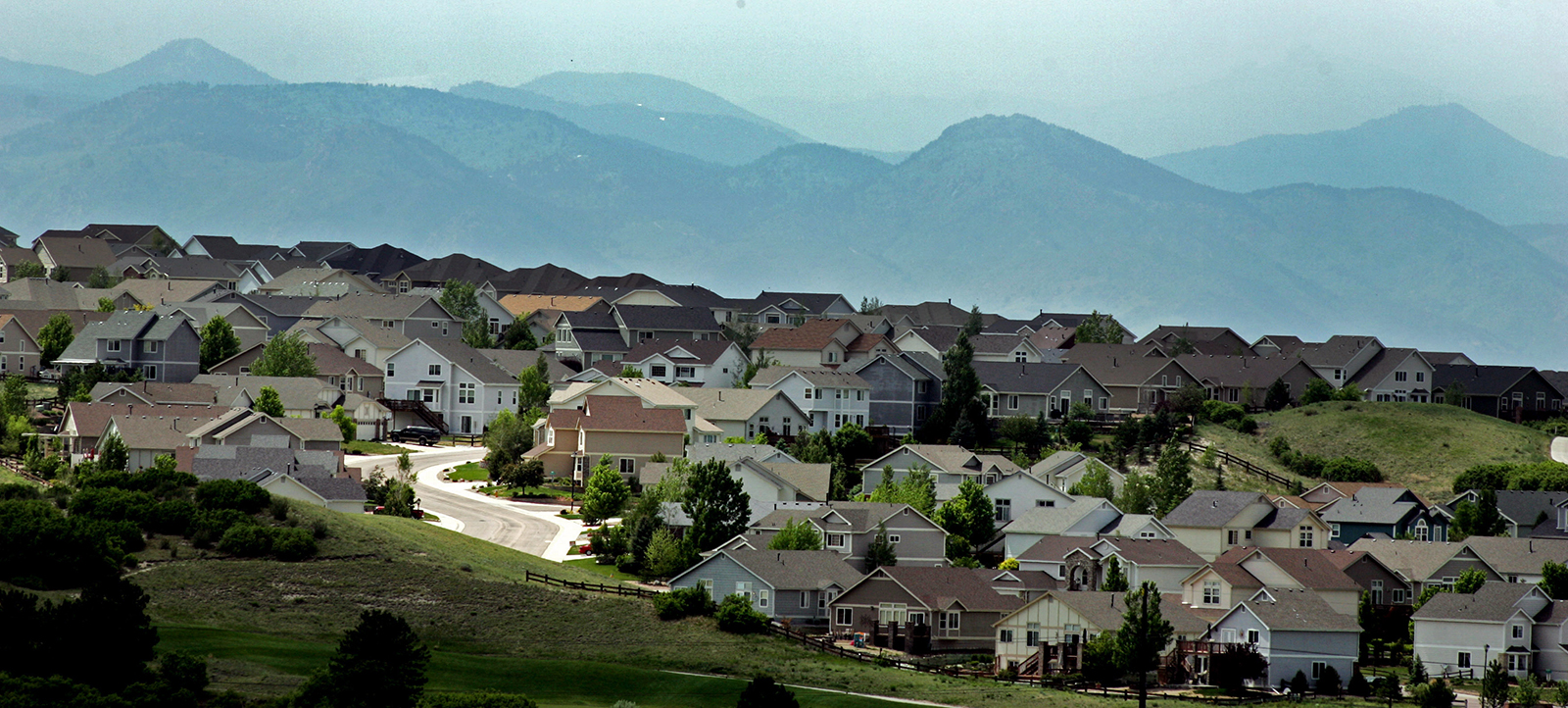 A neighborhood of single-family homes nestled against the foothills of the Rocky Mountains on a hazy day.