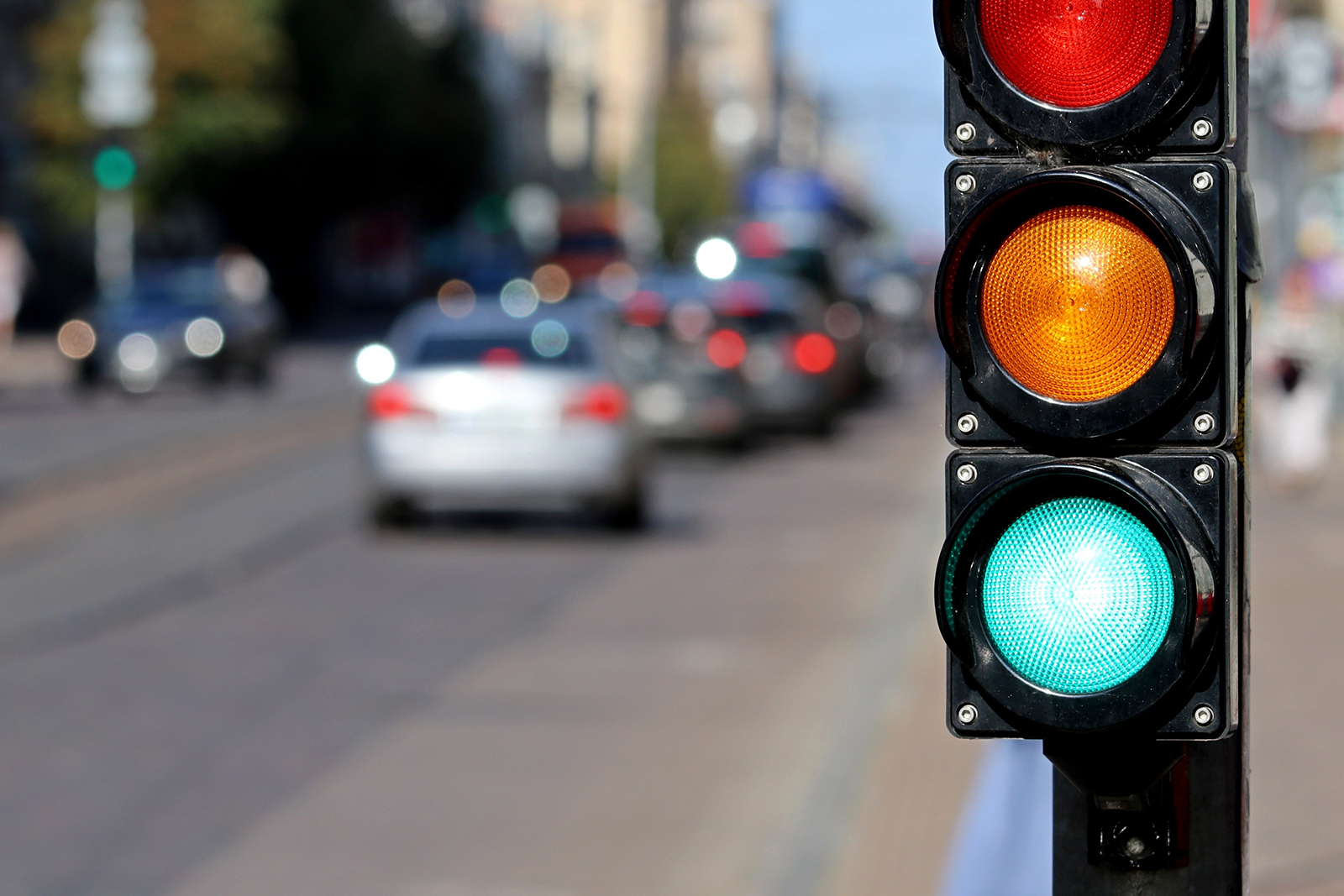 Cars proceed through a downtown intersection, with a green light in the foreground.