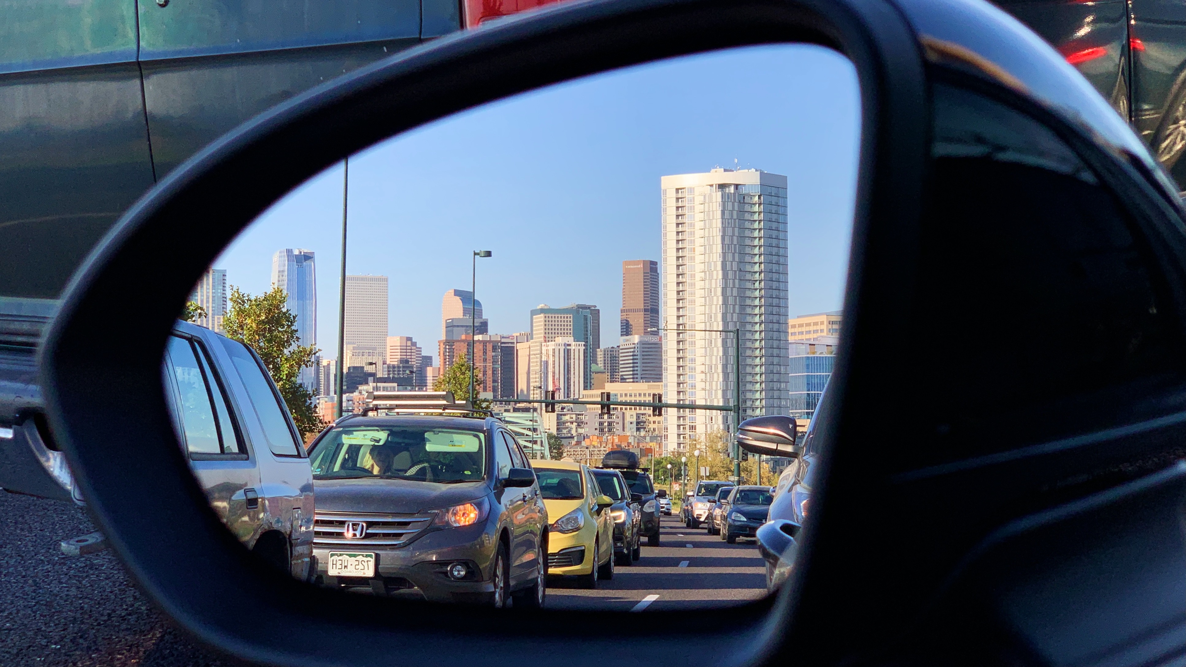 The downtown Denver skyline seen from the side-mirror of a vehicle. 