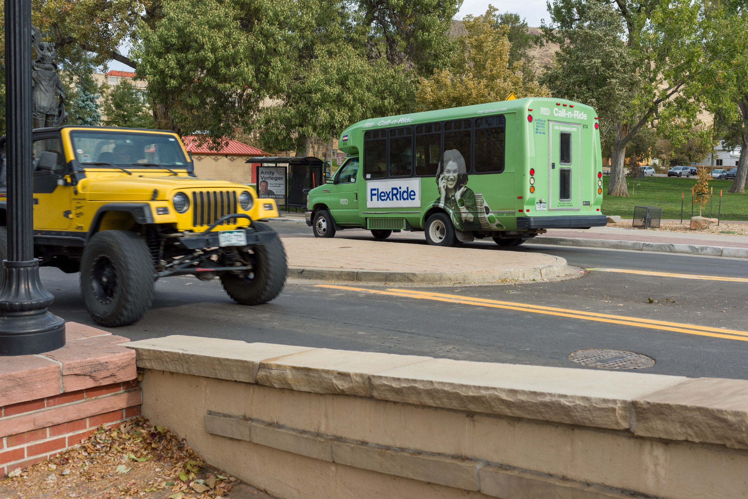 A yellow jeep travels on a busy street with a paratransit bus in the background.